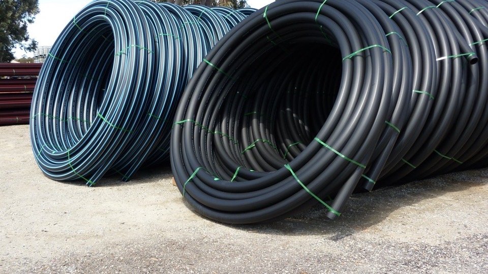 Coils of black HDPE irrigation pipe with blue stripes in a pipe yard