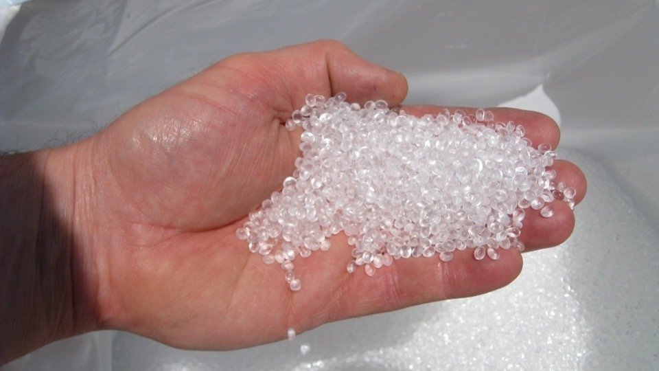 Handful of clear recycled polyethylene granules held over a bulk bag